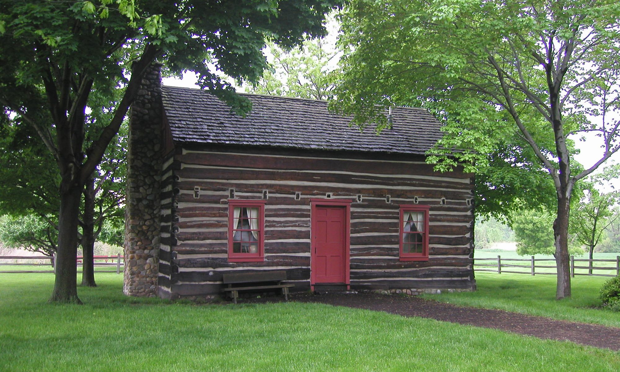 Image of a brown log cabin with red trim around the windows and a red door