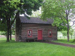 Image of a brown log cabin with red trim around the windows and a red door