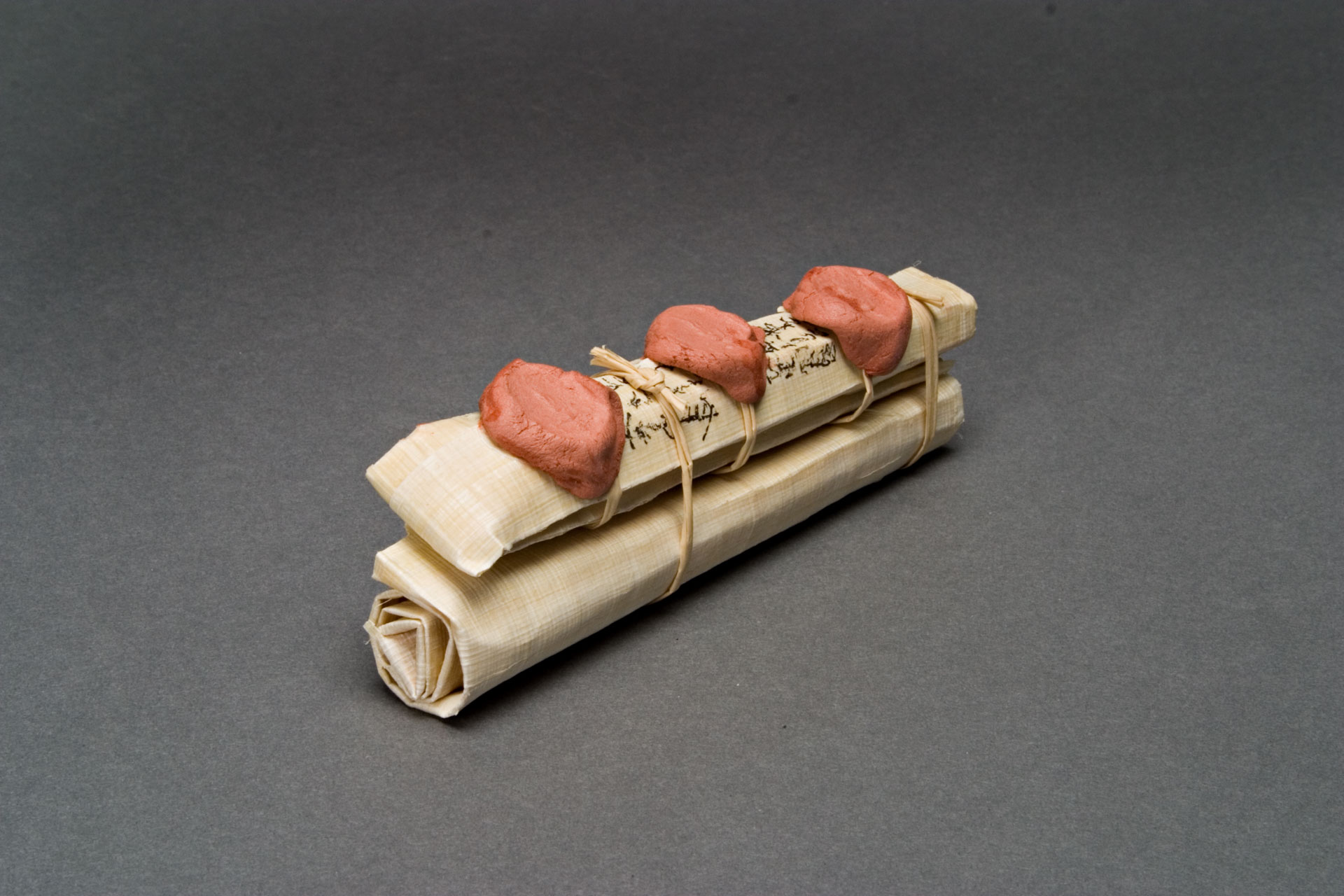 A scroll of papyrus is wound with twine, and three red-orange wax seals are on top of it.