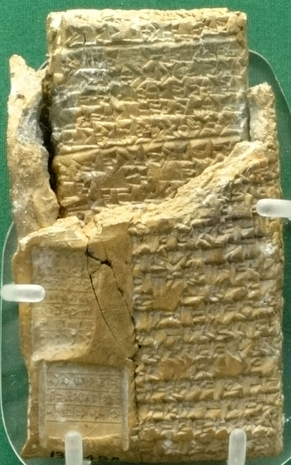 A tan-yellow clay enclosure with cuneiform writing on it has been broken and part of the top removed to reveal a clay tablet inside. Both the enclosure and the tablet are engraved with cuneiform writing.
