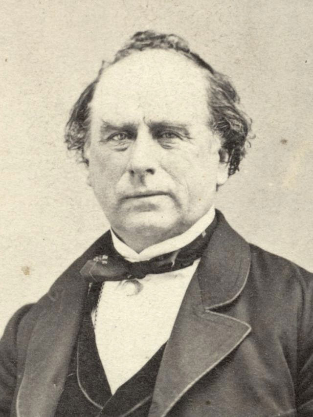 A photo of Edward Hunter. He has a rounder face, with darker hair, and is balding. He wears a midtone coat, dark vest, white shirt, and dark tie.