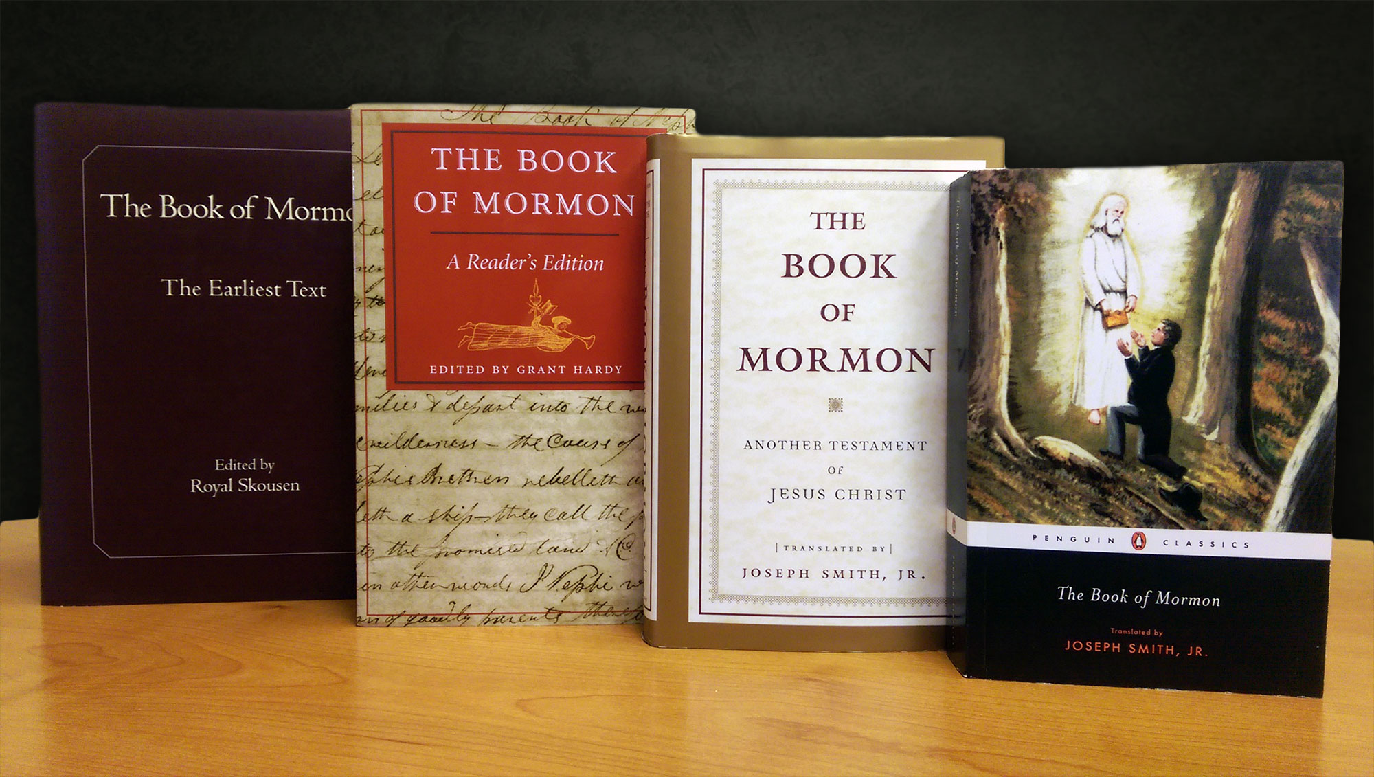 Four copies of The Book of Mormon stand up on a table, each of them from a different publisher.