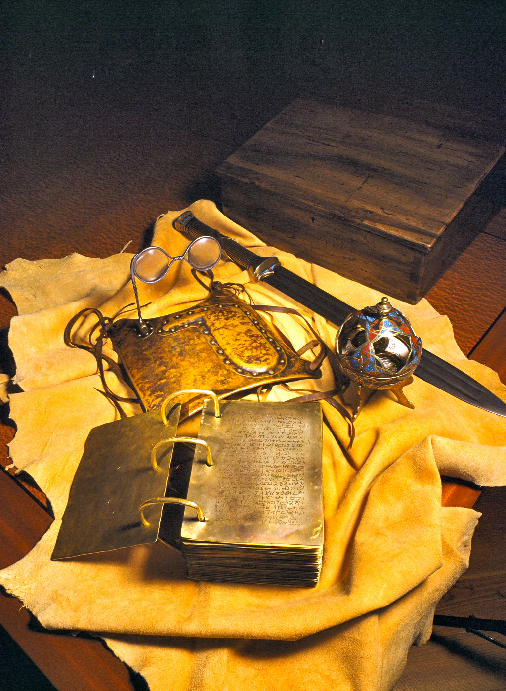 Several facsimiles of Book of Mormon artifacts sit on a piece of what looks like animal leather. The facsimiles include the breastplate with the Urim and Thummim, the sword of Laban, the Liahona, and the golden plates.
